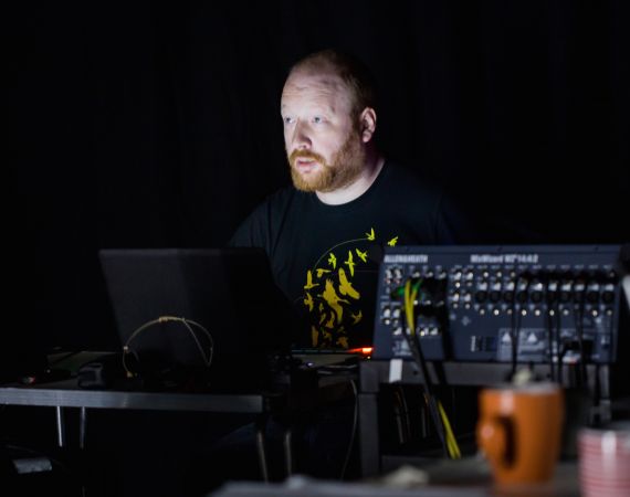 Tim sits in the dark lit only by a laptop screen, looking ghostly