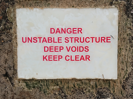 Image of a sign that reads: Danger, Unstable Structure, Deep Voids, Keep Clear