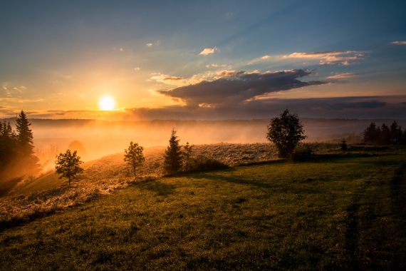 an image of a bright orange sunset, setting over rolling green hills