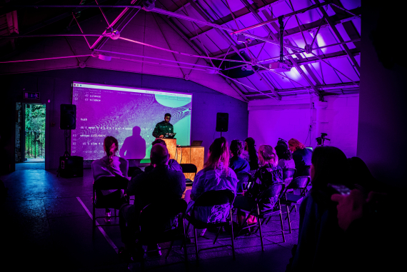 An image of a person delivering a talk, in a purple hued room