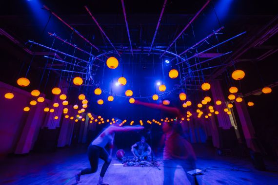 Musicians play in a room full of hanging colourful lightbulbs