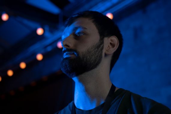 Image of a close up of a mans face against a blue background with fairy lights above