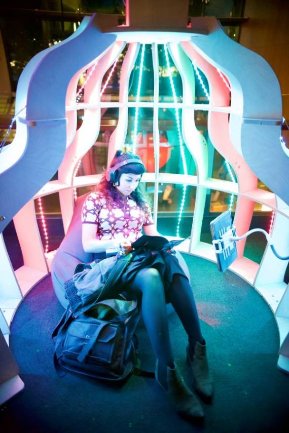 A person sits inside the brightly coloured Joey Pod, with headphones on and a bag at their feet
