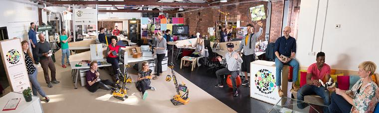A number of people spread around Pervasive Media Studio, each doing different things such as chatting with colleagues, showing work to colleagues, or posing with some of their work.