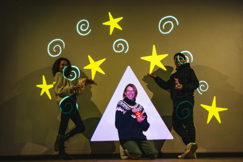 Team of three people smiling and pausing in front of colourful projected drawing