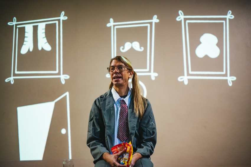 Performer sitting on border of the stage with projected drawings in the background